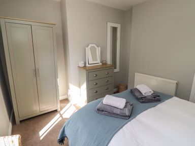 A bedroom with a bed with folded towels a wardrobe a chest of drawers and a mirror at Aln Cottage Alnmouth