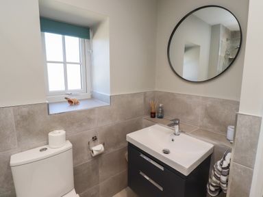 A bathroom with a toilet and a sink under a round mirror at Aln Cottage in Alnmouth