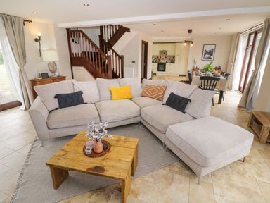 A living room with a beige sectional sofa and wooden coffee table near a staircase and an open kitchen and dining area at Little Acre in Church Lench near Harvington