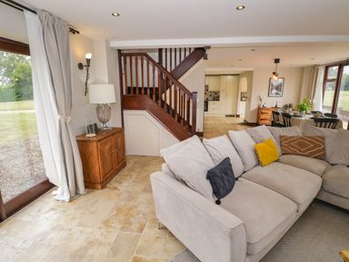 A living room with beige sofa and wooden stairs near a dining area at Little Acre in Church Lench near Harvington