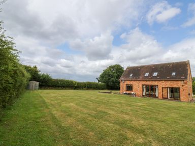 A large lawn with a brick house and shed under a cloudy sky at Little Acre in Church Lench near Harvington