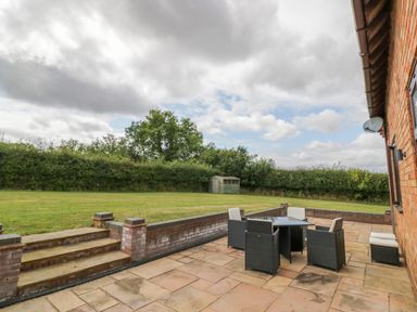 A patio with outdoor furniture and stairs leading to a lawn with a shed at Little Acre in Church Lench near Harvington