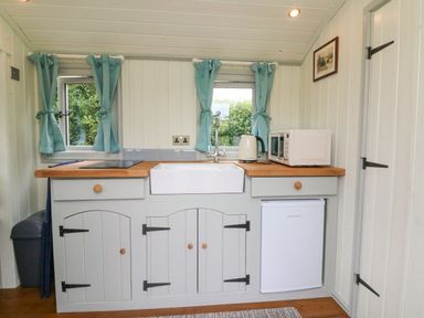 A kitchen with a sink toaster microwave small fridge and blue curtains at Cuckoo's Nest in South Molton