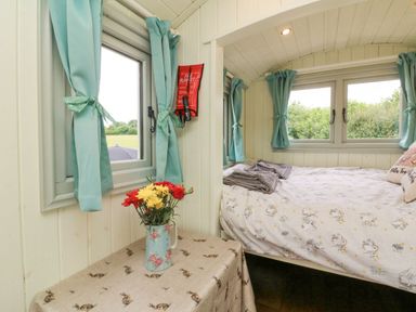 A bedroom with a bed near windows and curtains with a table and flowers at Cuckoo's Nest in South Molton