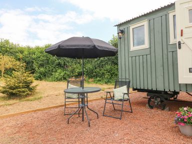 An outdoor seating area with a round table, two chairs with cushions, and a black umbrella next to a green wooden structure at Cuckoo's Nest in South Molton