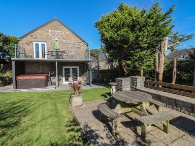 A backyard with a stone house balcony garden hot tub picnic table and wooden bench at Tremornah in Lamorna