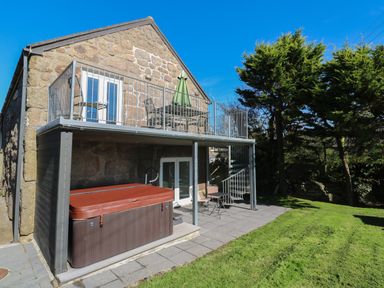 An outdoor area with a stone building balcony a hot tub and patio furniture at Tremornah in Lamorna