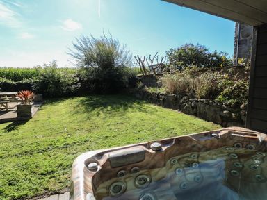 A garden with a hot tub in the foreground and a picnic table with plants on a patio at Tremornah in Lamorna