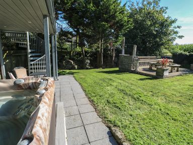 A backyard with a hot tub patio stone pathway grass and an outdoor seating area at Tremornah in Lamorna