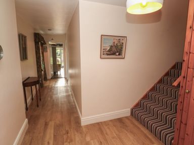 A hallway with wooden floor a striped carpeted staircase a small table and framed paintings at Tremornah in Lamorna