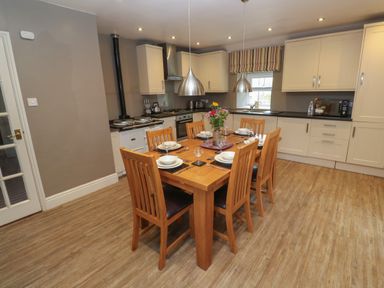A kitchen with wooden dining table and six chairs set with plates and glasses at Tremornah in Lamorna