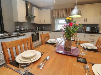 A kitchen with a wooden dining table set for four with flowers on a tray at Tremornah in Lamorna