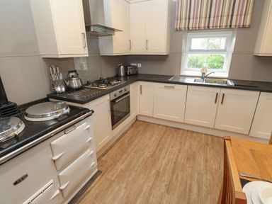 A kitchen with white cabinets a stove oven sink and wooden floor at Tremornah in Lamorna