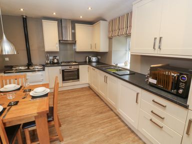 A kitchen with wooden dining table and chairs white cabinets microwave oven and stove at Tremornah in Lamorna