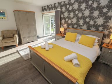 A bedroom with a double bed yellow pillows and throw a wardrobe and armchair at Tremornah in Lamorna