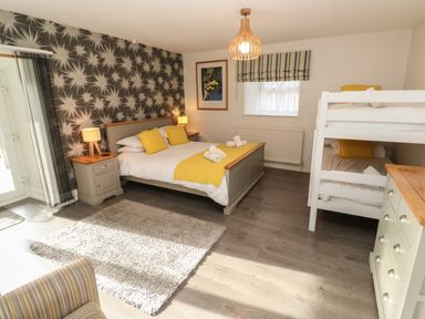 A bedroom with a double bed with yellow pillows and blanket beside a bunk bed a dresser and bedside tables at Tremornah in Lamorna