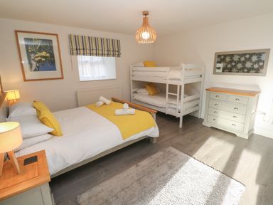 A bedroom with a double bed and bunk beds a dresser and nightstand with lamps at Tremornah in Lamorna