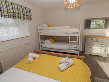 A bedroom with a double bed and bunk beds towels on beds chest of drawers and window with striped blind at Tremornah in Lamorna