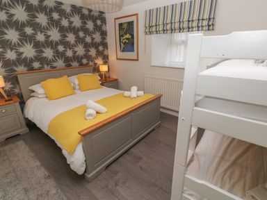 A bedroom with a double bed and bunk beds two bedside tables with lamps and a framed picture on the wall at Tremornah in Lamorna