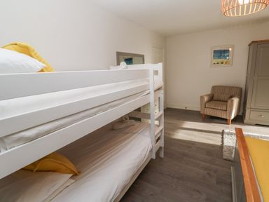 A bedroom with white bunk beds a striped armchair a grey wardrobe and a framed picture on the wall at Tremornah in Lamorna