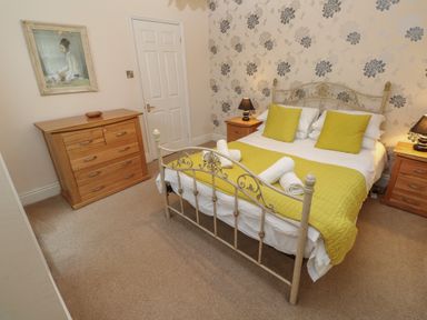 A bedroom with a metal bed frame a wooden dresser two bedside tables with lamps and floral wallpaper at Tremornah in Lamorna