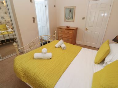 A bedroom with a yellow bedspread and pillows a wooden dresser a closed white door and a framed picture on the wall at Tremornah in Lamorna