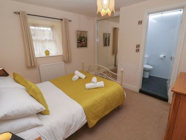 A bedroom with a double bed with yellow bedding and rolled towels a window with curtains a mirrored wardrobe and an open door to a bathroom at Tremornah in Lamorna