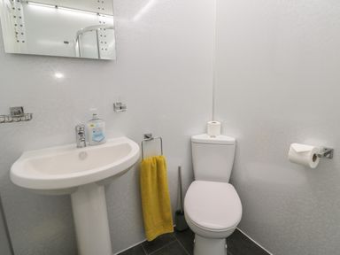 A bathroom with a sink a yellow towel a toilet and toilet paper at Tremornah in Lamorna