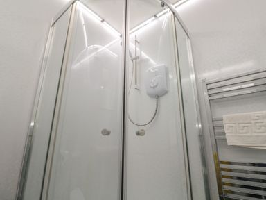 A shower enclosure with glass doors and a white electric shower unit next to a metal towel rack with a white towel at Tremornah in Lamorna