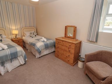 A bedroom with two single beds a wooden dresser with mirror a chair and a window at Tremornah in Lamorna