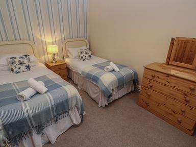 A bedroom with two single beds a wooden nightstand with a lamp and a wooden dresser with a mirror at Tremornah in Lamorna
