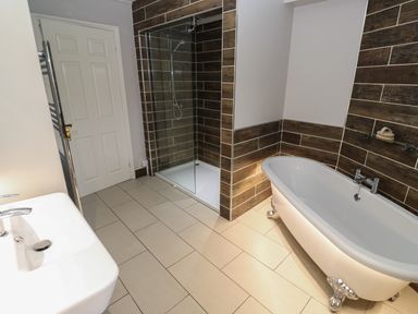 A bathroom with a freestanding tub a shower with glass door a sink and a closed door at Tremornah in Lamorna