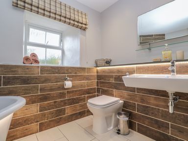 A bathroom with a toilet a sink a mirror towels on the window ledge and a trash bin at Tremornah in Lamorna