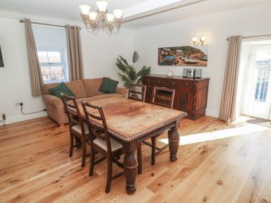 A dining room with a large wooden table and four chairs a sofa a wooden sideboard a plant and windows with curtains at Tremornah in Lamorna