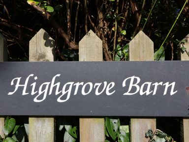 A wooden fence with a sign reading Highgrove Barn surrounded by leaves and branches at Highgrove Barn in Painswick