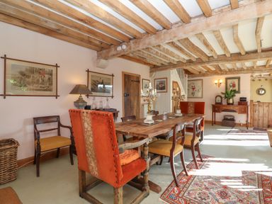 A dining room with a wooden table and chairs under exposed wooden beams at Highgrove Barn in Painswick