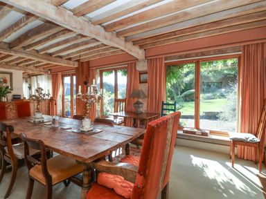 A dining room with a wooden table and chairs near large windows overlooking a garden at Highgrove Barn in Painswick