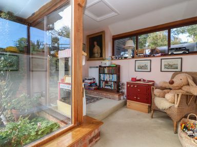 A playroom with a wicker chair and stuffed toy and a bookshelf with books by a window at Highgrove Barn in Painswick