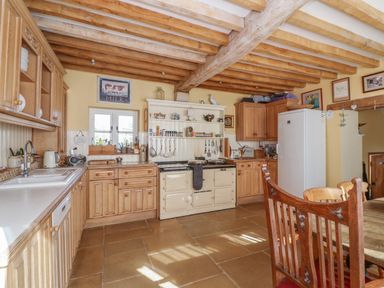 A kitchen with wooden cabinets wooden beams on ceiling a white cooker and a white fridge at Highgrove Barn in Painswick