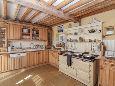 A kitchen with wooden cabinets and exposed beams with a large stove and utensils at Highgrove Barn in Painswick