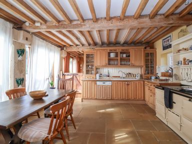 A kitchen with wooden cabinets dining table and chairs with a tiled floor at Highgrove Barn in Painswick