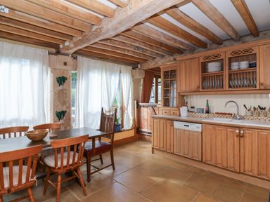 A kitchen with wooden cabinets a dining table with chairs and a door with white curtains at Highgrove Barn in Painswick