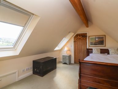 A bedroom with a wooden bed two skylight windows a wooden chest lamp on a nightstand and a wooden door at Highgrove Barn in Painswick