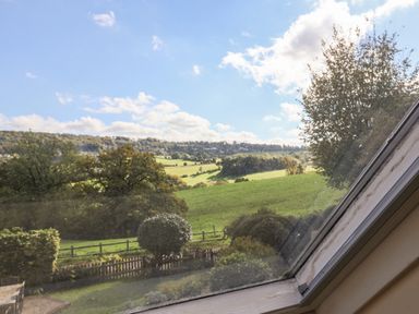 A view of green fields trees and a wooden fence through a window at Highgrove Barn in Painswick