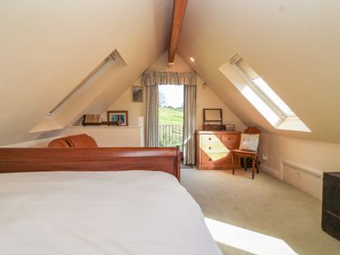 A bedroom with a wooden bed frame a chest of drawers a chair and windows on the slanted ceiling at Highgrove Barn in Painswick
