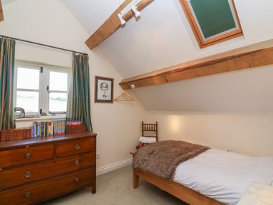 A bedroom with a single bed a wooden dresser books on the dresser a window with curtains and exposed wooden ceiling beams at Highgrove Barn in Painswick