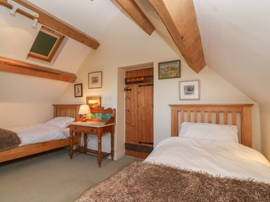 A bedroom with two single beds a wooden bedside table with a lamp wooden beams on the ceiling and framed pictures on the walls at Highgrove Barn in Painswick