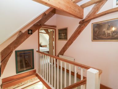 A hallway with wooden beams, paintings on walls, and a doorway leading to a bedroom at Highgrove Barn in Painswick