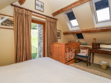 A bedroom with a white bed a wooden crib a wooden desk with a chair and two skylight windows at Highgrove Barn in Painswick