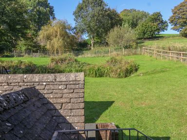 A grassy yard with a stone roof in the foreground and trees and fencing in the background at Highgrove Barn in Painswick